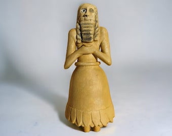 May include: A terracotta figurine of a standing figure with a long, braided beard and a long, flowing skirt. The figure has a simple, stylized face with large eyes and a small mouth.