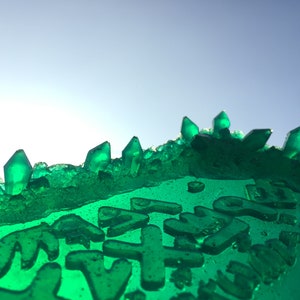 May include: A close-up of a green, translucent, crystal-like surface with a textured, bumpy surface. The surface is covered in small, green, translucent, crystal-like shapes. The surface is lit from the top, creating a bright, white light.