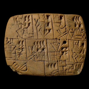 Puede incluir: Una tablilla de arcilla con escritura cuneiforme, un antiguo sistema de escritura utilizado en Mesopotamia. La tablilla es rectangular y de color marrón. La escritura está tallada en la superficie de la tablilla.