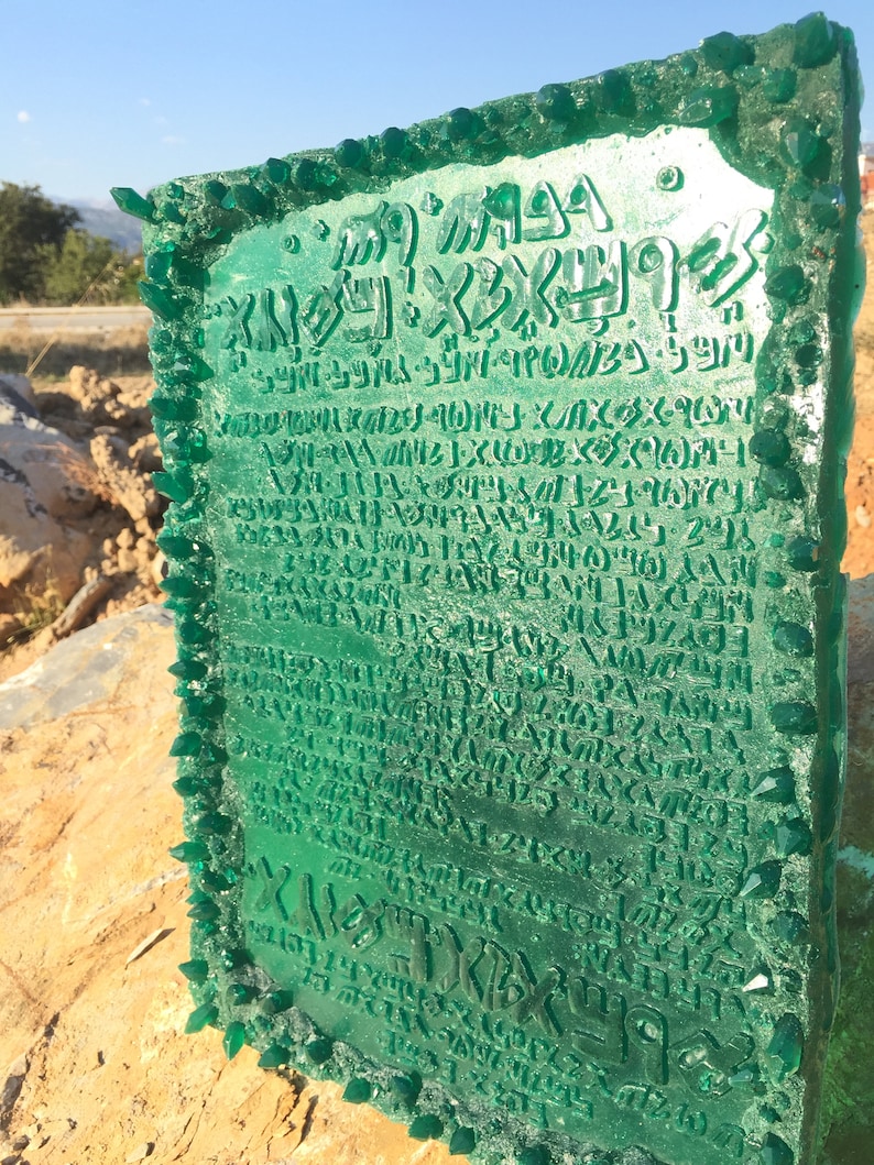 May include: A green glass plaque with a raised inscription in an ancient language. The plaque is surrounded by a border of green glass crystals.