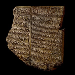 May include: A fragment of an ancient clay tablet with cuneiform script. The tablet is a light brown color and has a rectangular shape with a broken edge. The surface is covered in small, wedge-shaped marks.