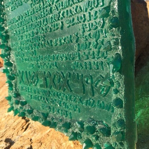 May include: A green glass plaque with a raised inscription and a border of green crystal-like points. The inscription is in an unknown language.