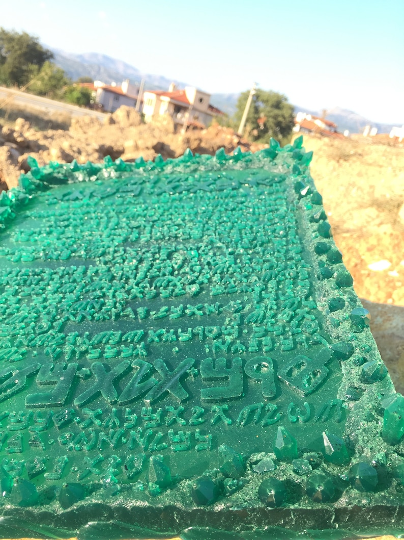 May include: A green resin plaque with a raised design of a script. The plaque is surrounded by a border of green crystals.