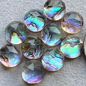 May include: A collection of iridescent, faceted glass beads. The beads have a round shape with multiple flat surfaces, creating a sparkling effect. The colors shift from blue to green and purple, reflecting light.