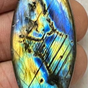 May include: A marquise-shaped labradorite gemstone with a vibrant display of colors. The stone features a mix of blues, yellows, and blacks, with a shimmering, iridescent effect. The polished surface showcases natural patterns and inclusions.