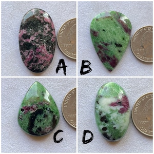 May include: Four polished ruby zoisite gemstones in various shapes. The stones display a mix of green, pink, black, and white colors. A quarter coin is placed next to each stone for size comparison. The gemstones are labeled A, B, C, and D.