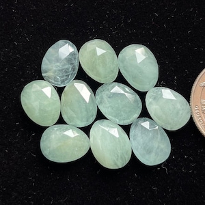 May include: Ten faceted aquamarine gemstones in a light blue-green color. The stones are oval shaped and have a smooth, polished finish.