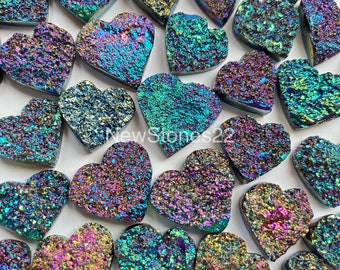 Op de afbeelding: Een verzameling van regenboogkleurige hartvormige stenen met een ruw, getextureerd oppervlak. De stenen zijn een mix van blauwe, groene, paarse en gouden kleuren.