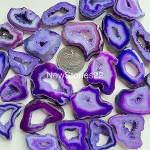 May include: A collection of purple agate slices with a natural hole in the centre. The slices are various sizes and shapes, and have a translucent, sparkly appearance.