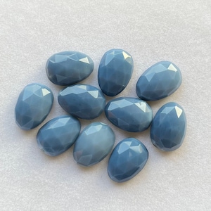 Puede incluir: Diez piedras preciosas ovaladas lisas de color azul claro. Las piedras tienen una apariencia facetada, casi iridiscente.