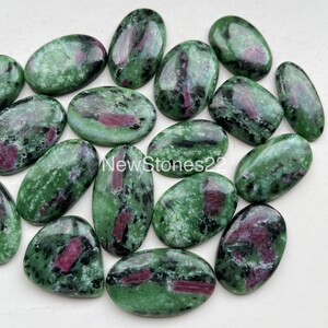 May include: A collection of 15 oval-shaped green zoisite gemstones with red and black inclusions. The stones are smooth and polished.