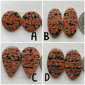 Op de afbeelding: Vier paar gepolijste rood-zwarte jaspis cabochons in verschillende vormen: rond, ovaal en peer. De cabochons zijn gerangschikt in vier rijen, gelabeld A, B, C en D.