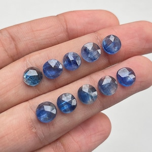 May include: Ten round, faceted, blue gemstones. The gemstones are arranged in two rows of five, with the top row slightly offset from the bottom row.