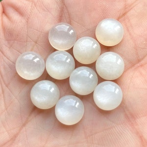 May include: A collection of ten white, round, iridescent moonstone cabochons. The stones have a smooth, polished surface and a subtle shimmer.