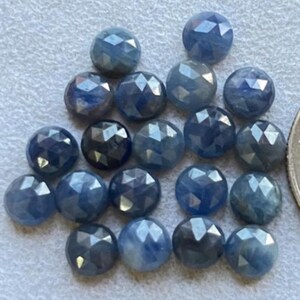 Puede incluir: Una colección de 20 piedras preciosas de zafiro azul facetadas. Los zafiros son redondos y tienen un corte facetado. Son de color azul medio y tienen un ligero brillo.