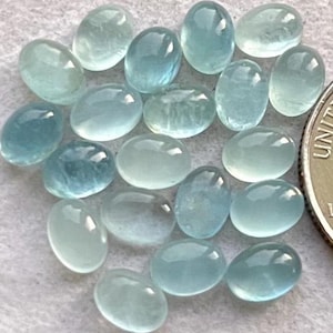 May include: A collection of oval-shaped aquamarine gemstones, ranging in size and shade of blue. The stones are smooth and polished, with a translucent appearance.