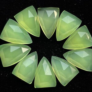 May include: Ten green gemstone cabochons in a triangle shape, arranged in a circle on a black background. A US quarter is included for size reference.