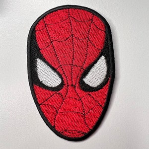 May include: Red and black embroidered patch of a superhero's mask with white eyes. The mask has a spider web design.
