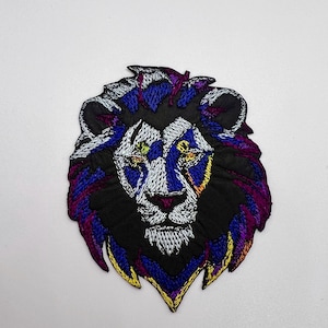 May include: Embroidered lion head patch with a black background and colorful mane. The lion's eyes are yellow and blue, and the mane is purple, blue, and yellow.