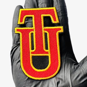 May include: Red and yellow embroidered iron-on patch with the letter "U" in a bold, blocky font.