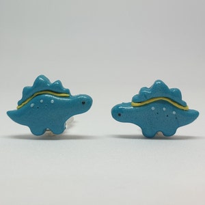 Cute turquoise little girls dinosaur - stegosaurus clip on earrings for unpierced ears in womens hands to show their size in real life, which is 2x1.4 cm or 0.79x0.55 inch.