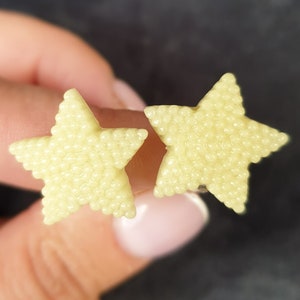 May include: A pair of yellow star-shaped earrings. The earrings are made of small beads that create a textured surface.