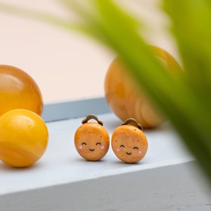 Könnte beinhalten: Ein Paar braune Ohrringe aus Ton in Form von lächelnden Keksen mit einem goldfarbenen Metallhaken.