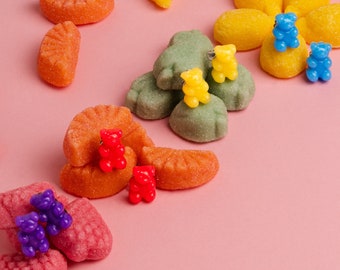 May include: Assortment of colorful gummy candies shaped like bears and fruit slices. The candies are arranged on a pink background.