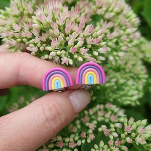 Woman holds Rainbow ear clips in her hands, showing their size in reel life. The size is little bit smaller that the width of the index finger.