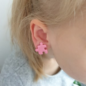Light pink puzzle piece earrings in non pierced ear of a 6 year old blonde girl.