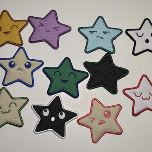 May include: A collection of eleven star-shaped embroidered patches with various facial expressions. The patches are in a variety of colors, including yellow, purple, blue, white, green, and black. Each star has a black outline.