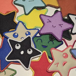 May include: A collection of colorful star-shaped patches with embroidered details. The patches feature various colors, including black, red, blue, yellow, and green, with embroidered faces and expressions. These patches are suitable for clothing or accessories.