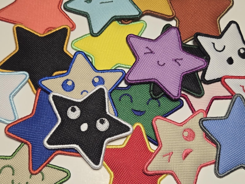 May include: A collection of colorful star-shaped patches with embroidered details. The patches feature various colors, including black, red, blue, yellow, and green, with embroidered faces and expressions. These patches are suitable for clothing or accessories.
