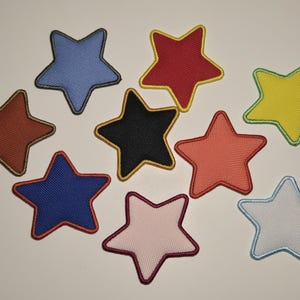 May include: A collection of ten star-shaped patches in various colors, including blue, red, yellow, and black. Each patch has a contrasting border, and a mesh-like texture.
