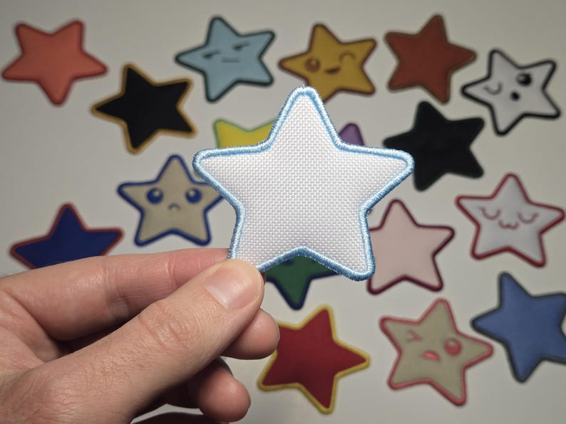 May include: A white star-shaped patch with a light blue border is held in front of a collection of colorful star patches. The patches have various colors and facial expressions, including blue, yellow, red, and black.