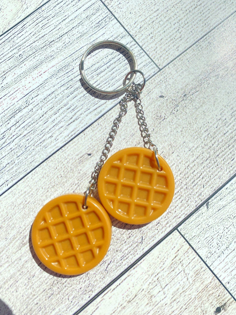 May include: A keychain with two round, brown waffle-shaped charms attached to a silver chain and ring.