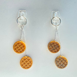 May include: Two pairs of earrings with silver chains and round, brown waffle-shaped charms.