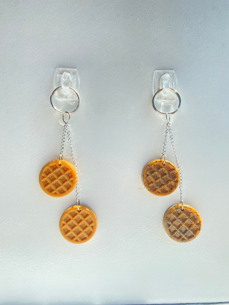 May include: Two pairs of earrings with silver chains and round, brown waffle-shaped charms.