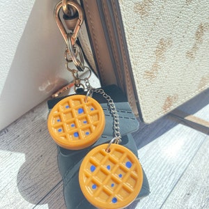 May include: A gold chain keychain with two round, brown waffle-shaped charms. The charms have blue dots on them.