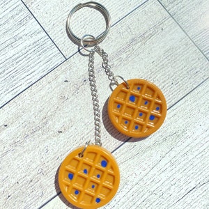May include: A keychain with two waffle-shaped charms. The charms are brown with blue spots and are attached to a silver chain and ring.