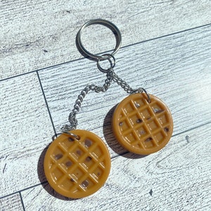 May include: A keychain featuring two brown waffle-shaped charms connected by a silver chain and ring.