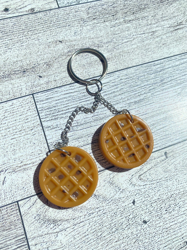 May include: A keychain featuring two brown waffle-shaped charms connected by a silver chain and ring.