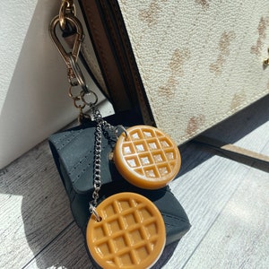 May include: A black zippered pouch with a silver chain attached to two brown waffle-shaped charms. The charms are hanging from the chain.