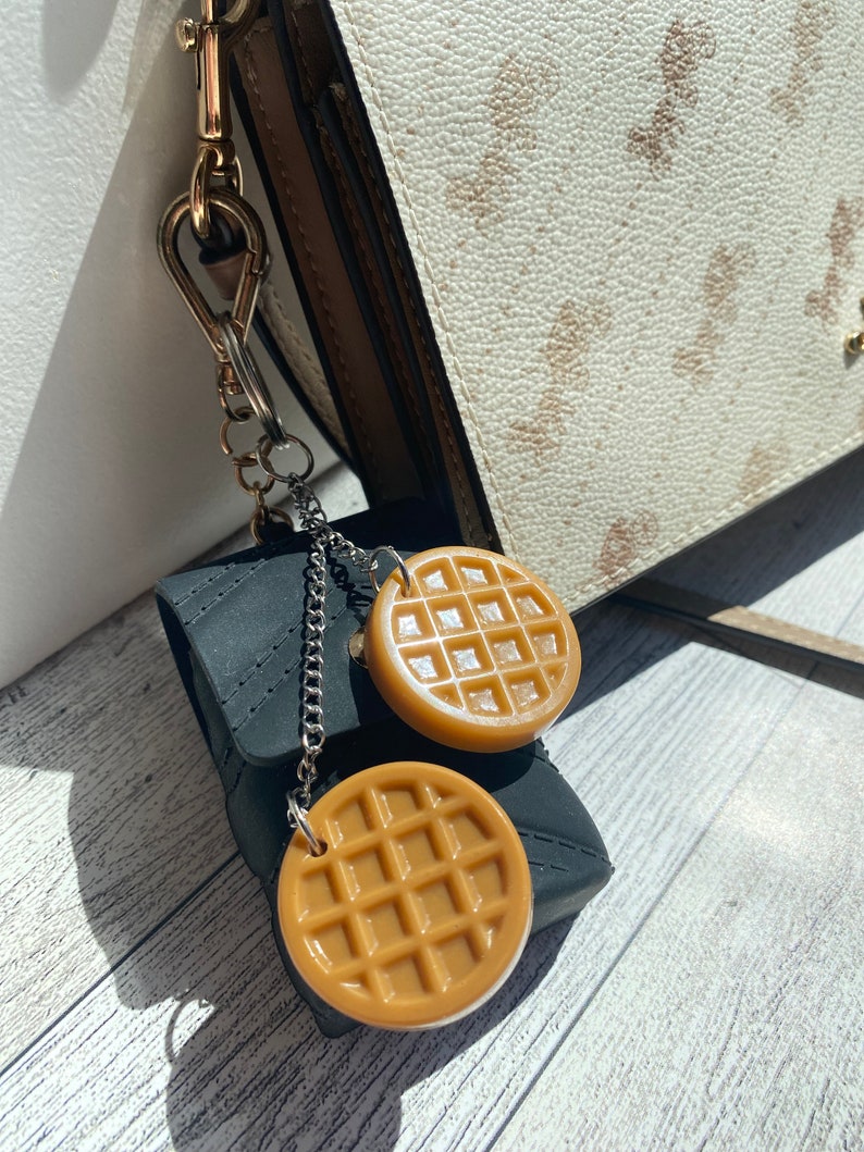 May include: A black zippered pouch with a silver chain attached to two brown waffle-shaped charms. The charms are hanging from the chain.