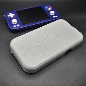 May include: A handheld gaming console in a deep blue color, with a black screen and colorful buttons. A light gray case with the embossed text "ANBERNIC" is in the foreground. The console has white buttons and a directional pad.