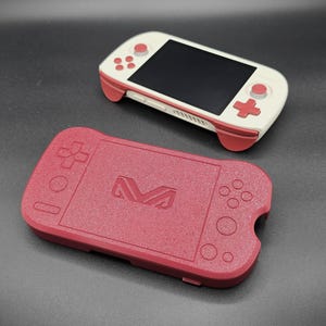 May include: A handheld gaming console with a white body and red accents, featuring a black screen and control buttons. A matching red case with a textured surface and a stylized "M" logo is also present.