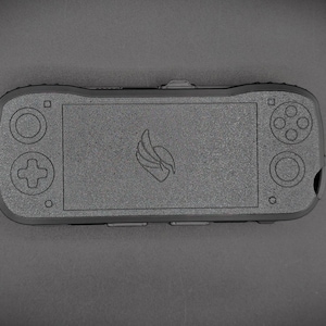 May include: A handheld gaming device in a dark gray color. The device features a screen in the center, with a directional pad and buttons on the left and right sides. A logo is centered on the screen.