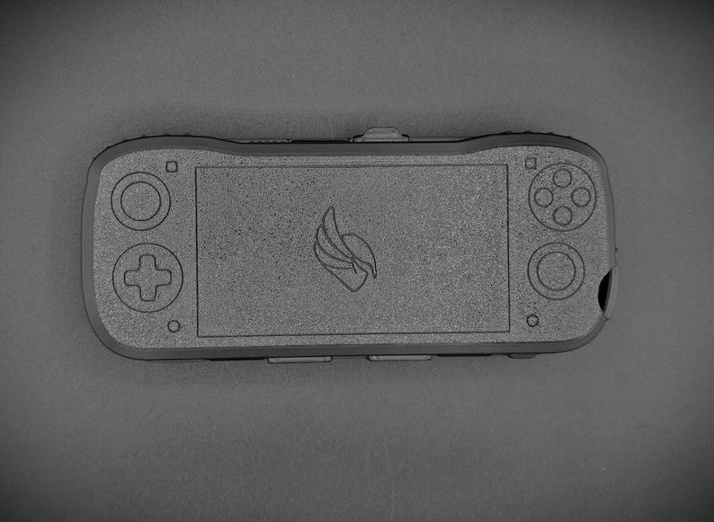May include: A handheld gaming device in a dark gray color. The device features a screen in the center, with a directional pad and buttons on the left and right sides. A logo is centered on the screen.