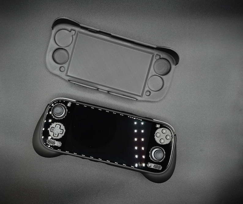 May include: Two handheld gaming consoles, one in a gray protective case and the other with a black screen and controls. The consoles are set against a dark gray background, showcasing their design and features.