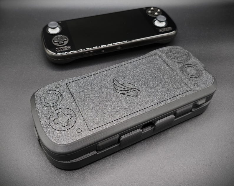 May include: Two black handheld gaming devices are displayed. One is a sleek, modern console with a screen and buttons. The other is a textured case with a controller layout and a logo. The case appears to be designed to protect the console.